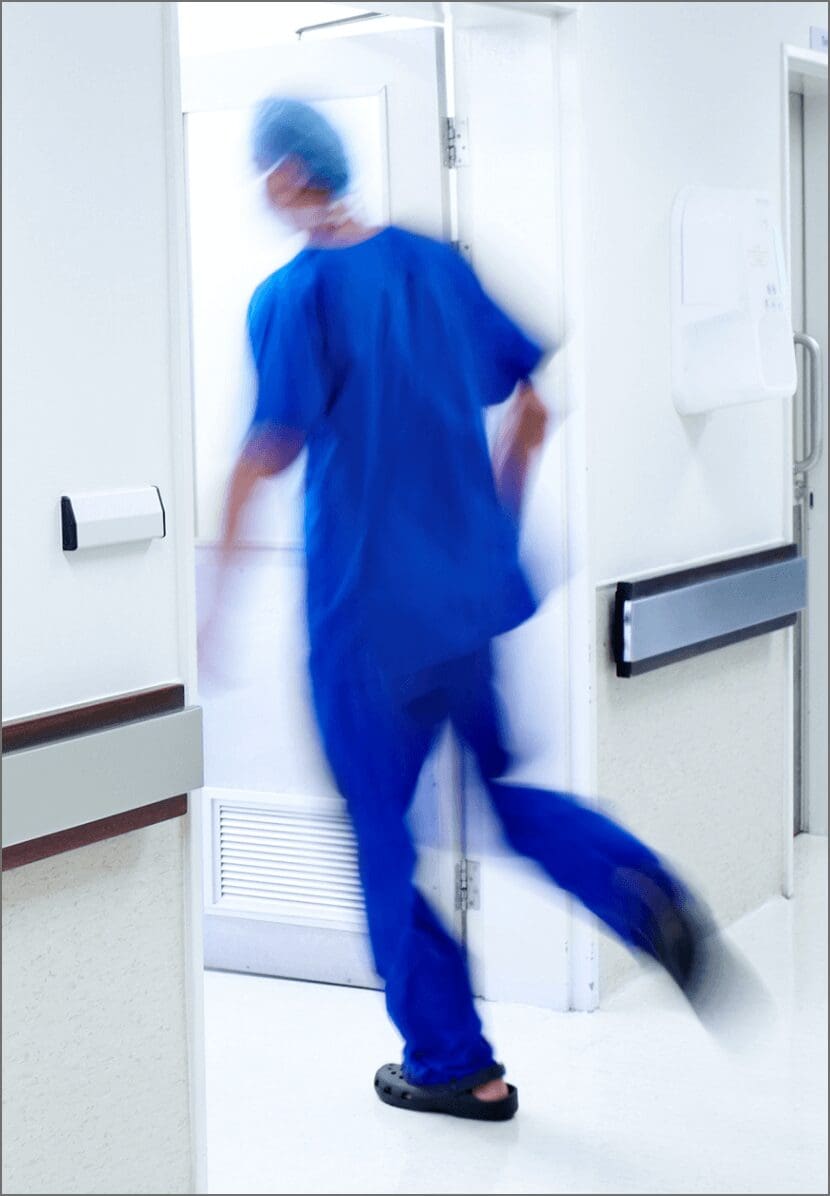 A medical professional in blue scrubs quickly entering a hospital room and getting an alert on a Relay device.