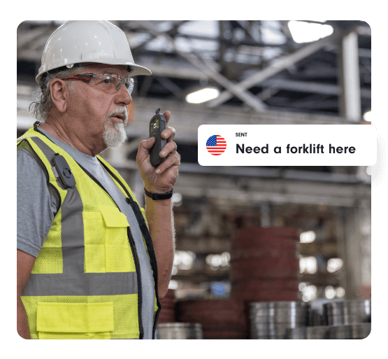 Industrial worker wearing a hard hat and safety vest uses a Relay device to communicate in a warehouse. A caption overlay shows a translated message: “Need a forklift here” with a U.S. flag icon.