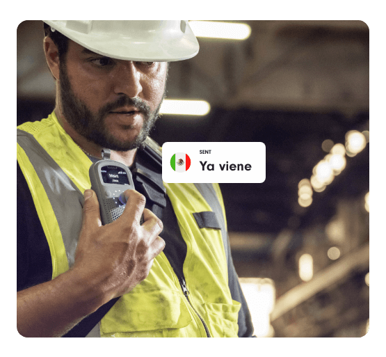 Industrial worker in a hard hat and safety vest speaks into a Relay device. A message overlay with a Mexican flag icon reads “Ya viene,” meaning “It’s on the way.”