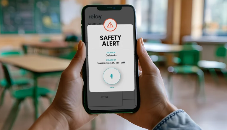 Hands holding a smartphone with the Relay app displaying a safety alert for the cafeteria, including the alert creator’s name and time.