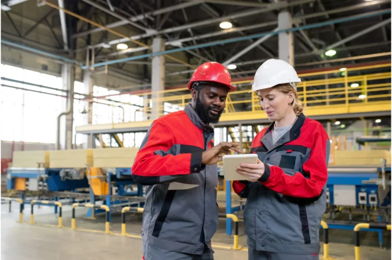 Manufacturing workers in red hats and jackets talking to about innovation on the shop floor