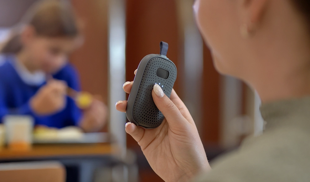 School staff member uses a Relay device in the cafeteria while children eat lunch in the background.
