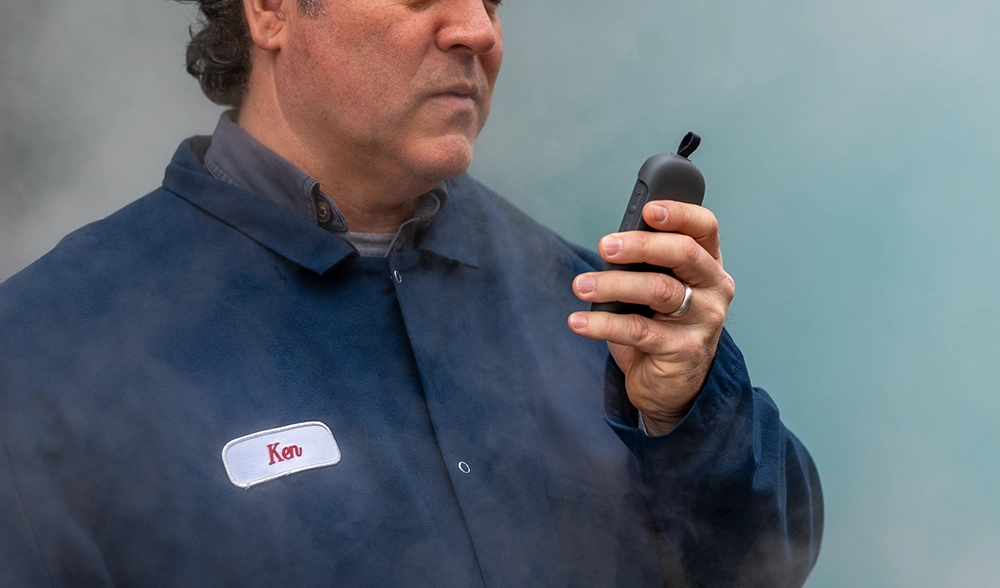 Worker wearing a blue uniform and name patch labeled "Ken" speaks into a Relay device while surrounded by steam.