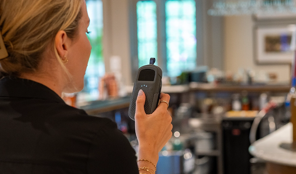 Food service employee holding Relay device to coordinate across kitchen and bar.