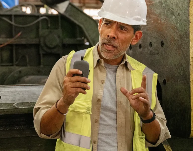 Factory worker in safety vest and hard hat communicating through RelayX device.