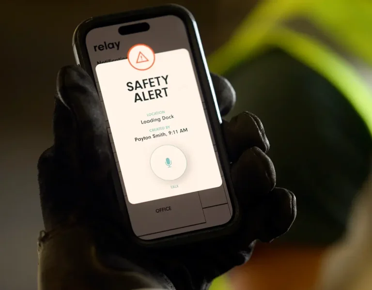 Worker holding a smartphone displaying a Relay safety alert for the loading dock.