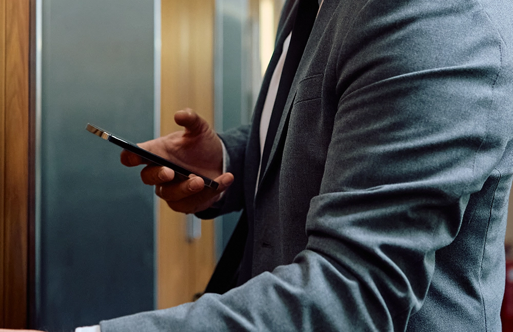 Hotel Manager in a suit holding a smartphone, checking the location of staff members on the Relay app.