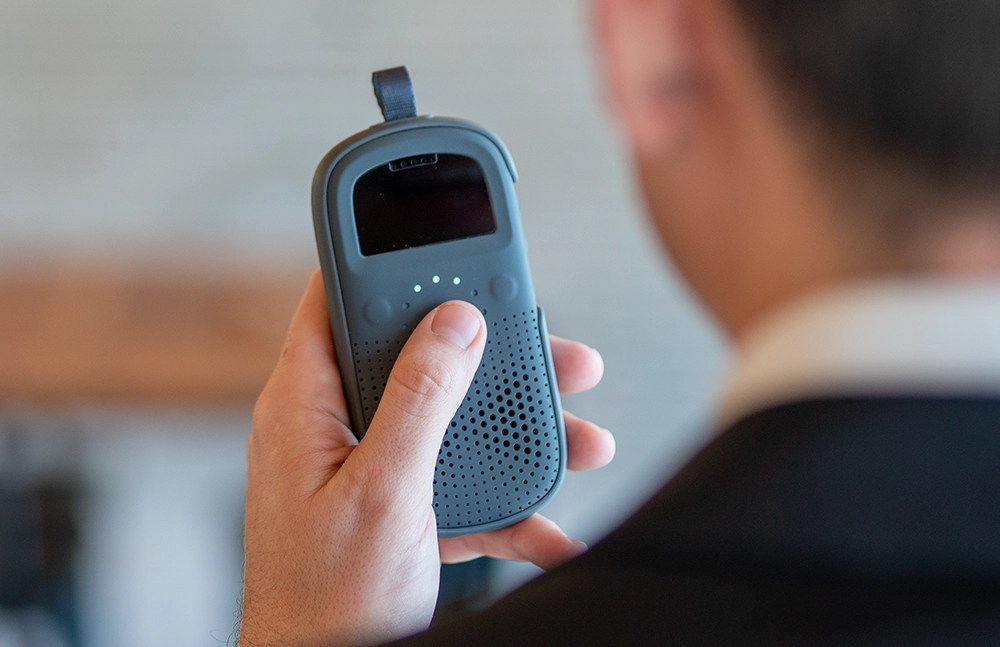 Person holding a RelayX device, listening as TeamTranslate translates an incoming message in real time.