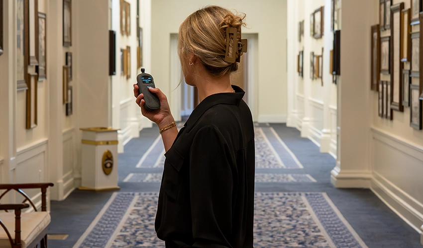 Event staff member using a Relay device in a large hallway lined with framed artwork.