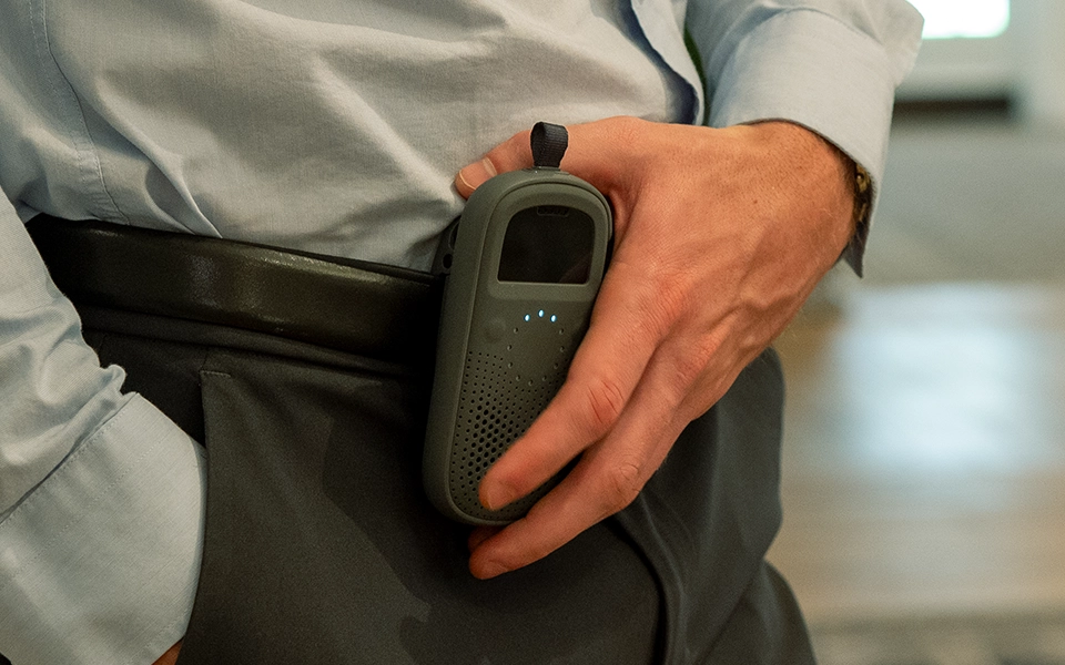 Person wearing business attire clipping a RelayX device to their belt for easy access.